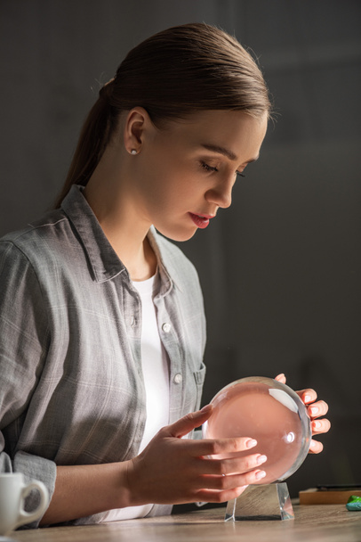 Side view of beautiful astrologer using crystal ball at table - Photo, Image