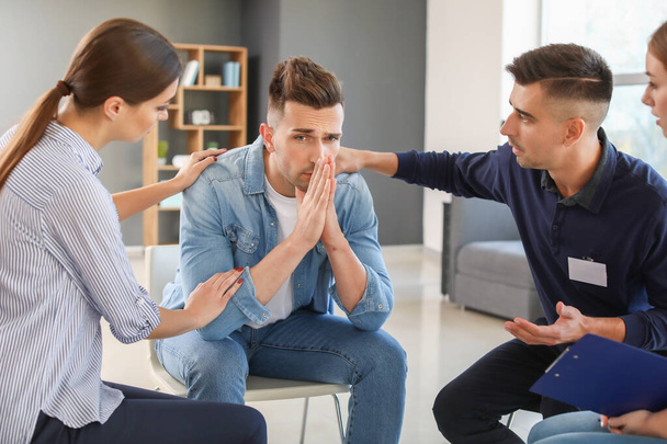 Young people calming sad man during psychological support session - Фото, изображение