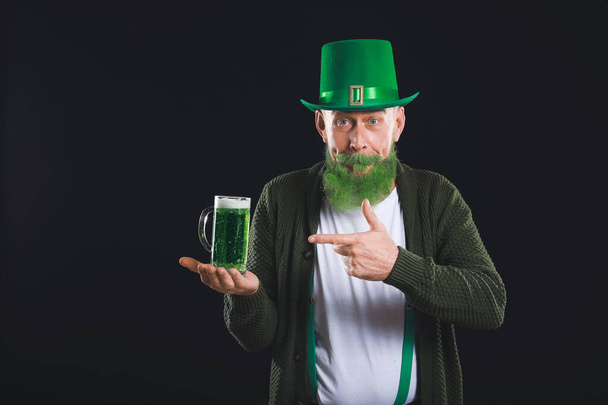 Funny mature man with glass of beer on dark background. St. Patrick's Day celebration - Фото, изображение