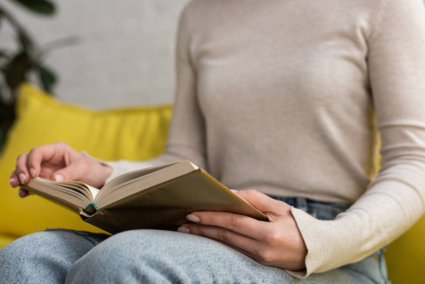 Cropped view of young woman reading book on couch - Foto, imagen