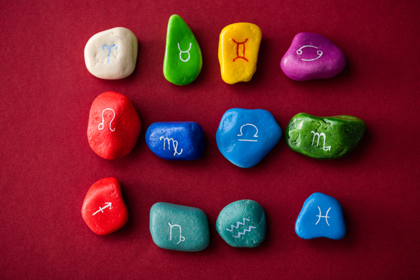 Верхний вид разноцветных камней с знаками зодиака на красной поверхности
 - Фото, изображение