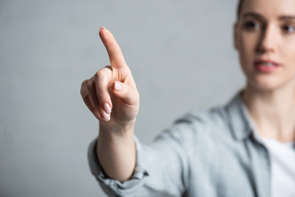 Enfoque selectivo de la mujer señalando con el dedo aislado en gris
 - Foto, Imagen