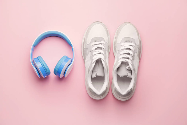 Stylish sporty shoes and headphones on color background - Foto, Bild