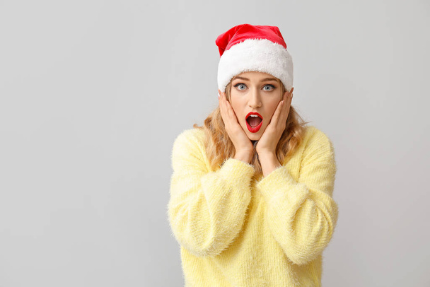 Surprised young woman in Santa hat on light background - Foto, afbeelding