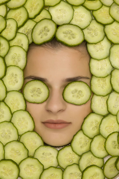 Jeune belle femme posant avec des tranches de concombre autour de son visage
 - Photo, image