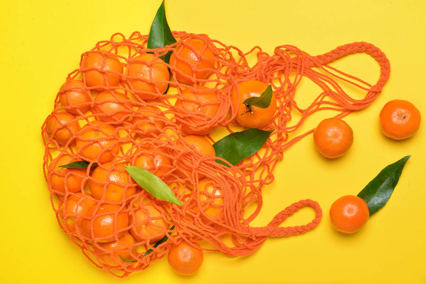 Сумка со сладкими мандаринами на цветном фоне
 - Фото, изображение