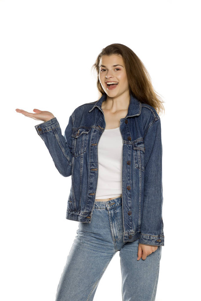Jonge mooie vrouw in jeans houden denkbeeldig object op haar hand op witte achtergrond - Foto, afbeelding
