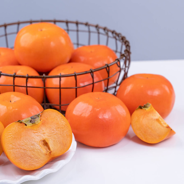 Fresh beautiful sliced sweet persimmon kaki isolated on white kitchen table with gray blue background, Chinese lunar new year design concept, close up. - Photo, Image