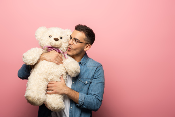 Handsome man kissing teddy bear on pink background with copy space - Photo, image