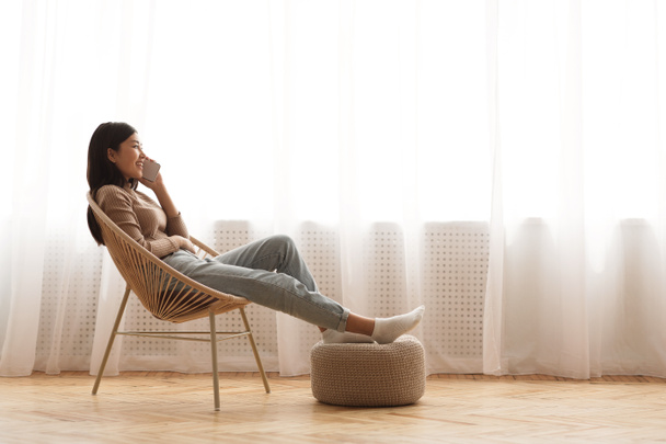 Chica adolescente relajándose en un sillón moderno y hablando por teléfono
 - Foto, Imagen
