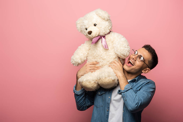 Excited young man looking at teddy bear on pink background - Foto, immagini