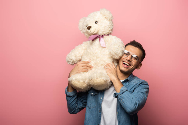 Smiling man holding teddy bear and looking at camera on pink background - Foto, Imagem