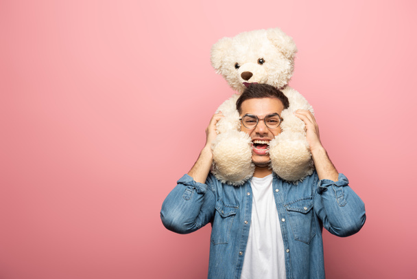 Laughing young man looking at camera while holding teddy bear on pink background - Fotografie, Obrázek