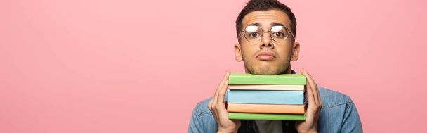 Panoramic shot of confused man with books looking at camera isolated on pink  - Photo, image
