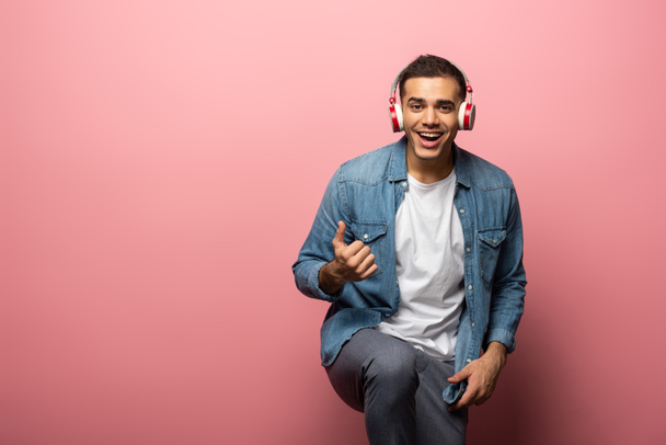 Man in headphones smiling at camera and showing like sign on pink background - Foto, immagini