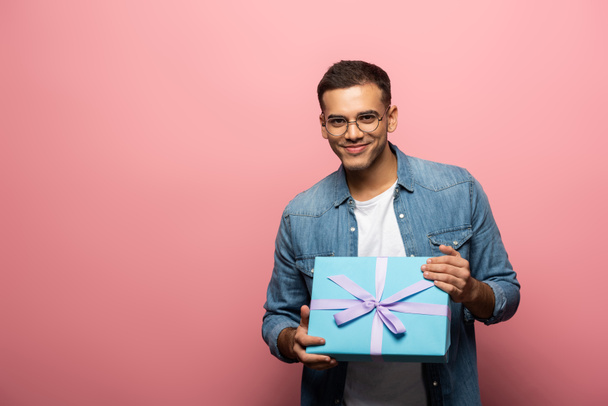 Young man holding gift and smiling at camera on pink background - Foto, afbeelding