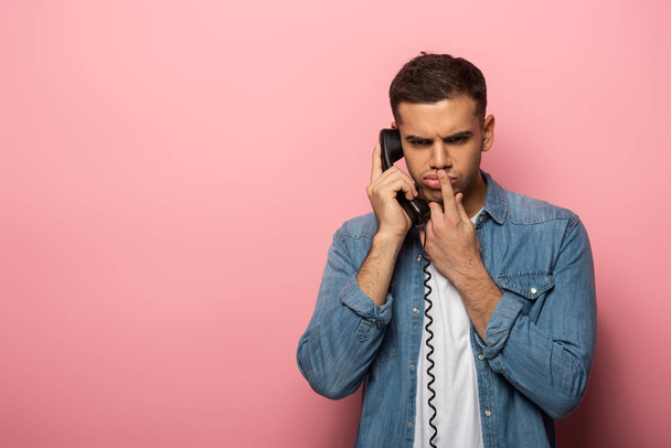 Átgondolt ember ujjal szájon át beszél telefonon rózsaszín háttér - Fotó, kép