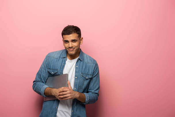 Handsome man holding laptop and smiling at camera on pink background - Φωτογραφία, εικόνα