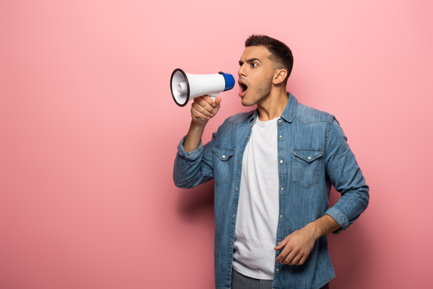 Side view of young man screaming in loudspeaker on pink background - Photo, Image