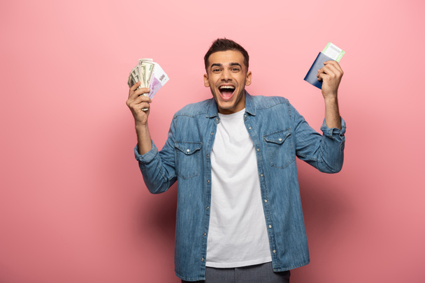 Ενθουσιασμένος άνθρωπος με μετρητά, διαβατήριο και κάρτα επιβίβασης σε ροζ φόντο - Φωτογραφία, εικόνα