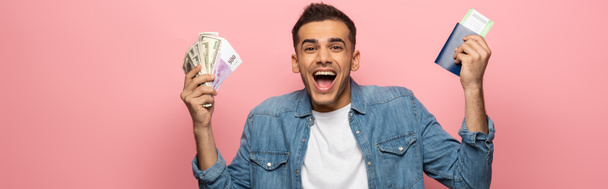 Panoráma felvétel izgatott férfi kezében készpénz, útlevél és beszállókártya rózsaszín háttér - Fotó, kép