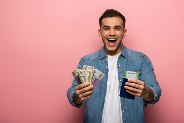 Überraschter Mann mit Bargeld, Bordkarte und Reisepass auf rosa Hintergrund - Foto, Bild