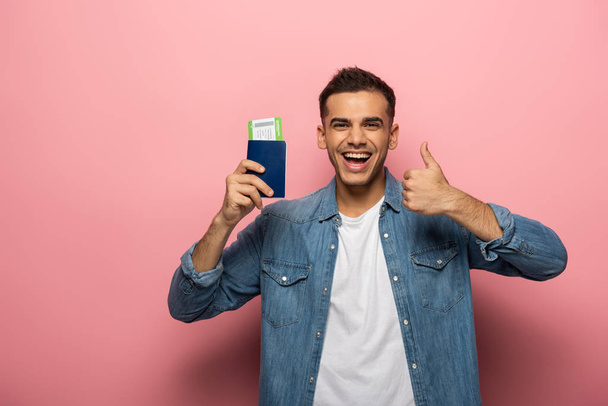 Hombre sonriente sosteniendo pasaporte con tarjeta de embarque y mostrando como signo sobre fondo rosa
 - Foto, imagen
