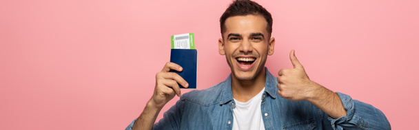 Panoramaaufnahme eines gut gelaunten Mannes mit Reisepass und Bordkarte, die wie ein Schild isoliert auf rosa  - Foto, Bild