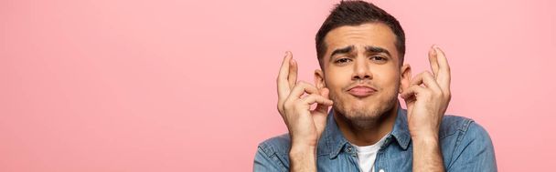 Panoramic shot of man with facial expression crossing fingers isolated on pink - Photo, Image