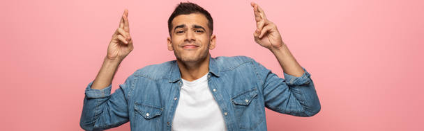 Panoramic shot of man with crossed fingers smiling at camera isolated on pink  - Foto, afbeelding