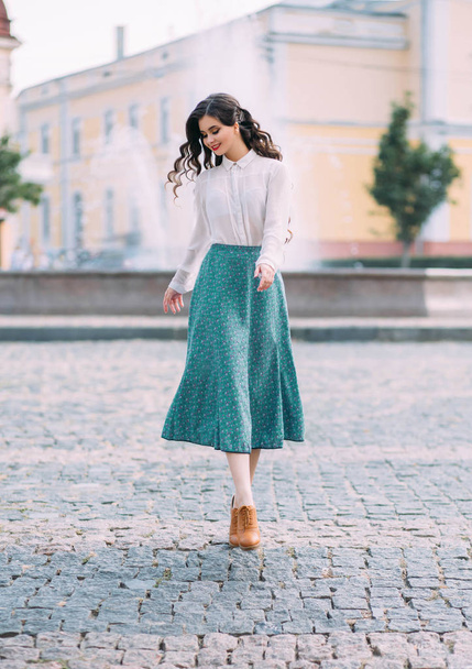 woman brunette student is walking around street city outdoors. Long wavy hair flying in motion. cheerful happy girl. face smile. white vintage blouse, mint midi skirt brown retro boots. floral print - Fotoğraf, Görsel