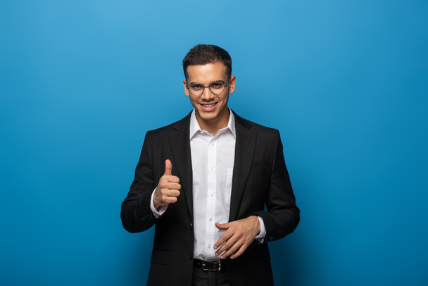 Homme d'affaires souriant montrant geste pouce vers le haut sur fond bleu
 - Photo, image