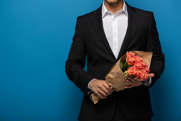 Cropped view of businessman holding bouquet on blue background with copy space - Фото, изображение