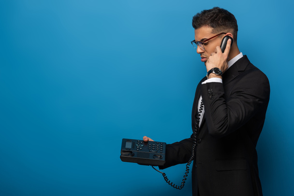 Side view of businessman talking on retro telephone on blue background - 写真・画像