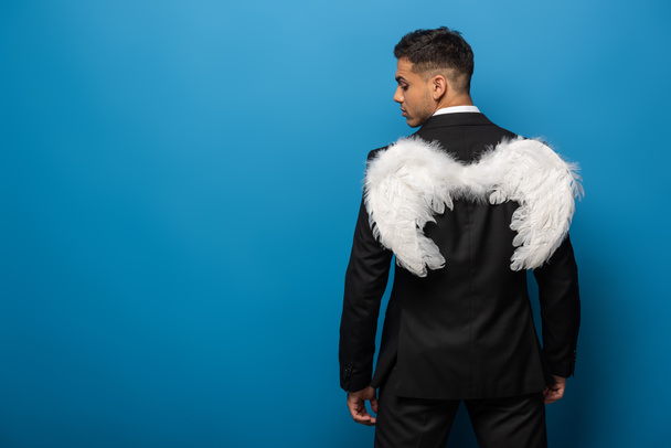 Back view of businessman with white wings on blue background - Photo, Image