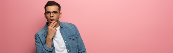 Panoramic shot of shocked man with hand by chin looking at camera on pink background - Photo, Image