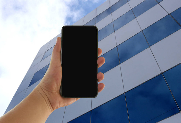 Mano del hombre con un teléfono inteligente en blanco en la alta ba edificio de negocios
 - Foto, imagen