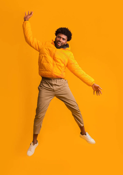 Joyful black man in winter jacket happily jumping up - Fotó, kép