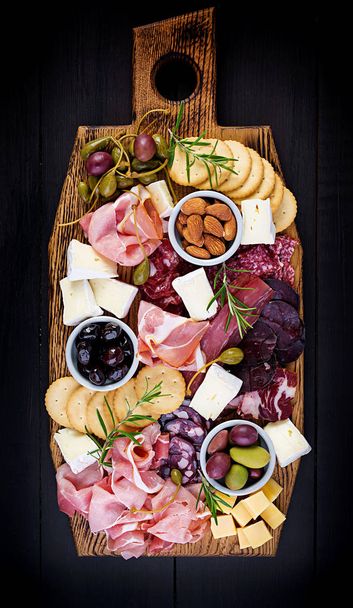 Antipasto platter with ham, prosciutto, salami, cheese,  crackers and olives on a wooden background.  Christmas table. Top view, overhead - Foto, imagen