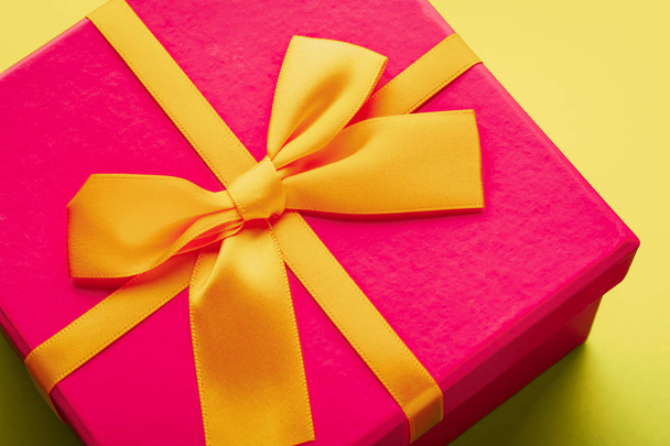 Close-up of a purple gift box with a yellow ribbon tied with a bow on a yellow background - Photo, Image