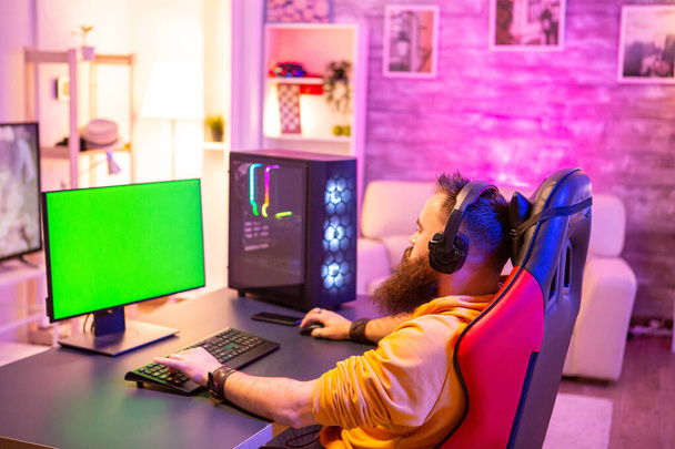 緑の画面のコンピュータ上のネオンの部屋で強力なゲームPCで遊んでいる男 - 写真・画像