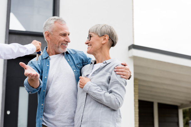 cropped view of broker giving keys of new house to smiling mature man and woman  - Foto, afbeelding