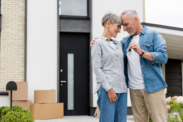 mature man holding keys of new house and hugging smiling woman  - Фото, зображення