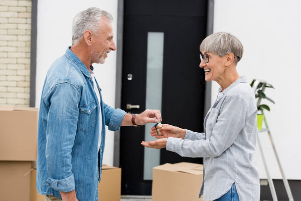 widok z boku Dojrzałe mężczyzna dając klucze nowy dom dla uśmiechnięta kobieta  - Zdjęcie, obraz
