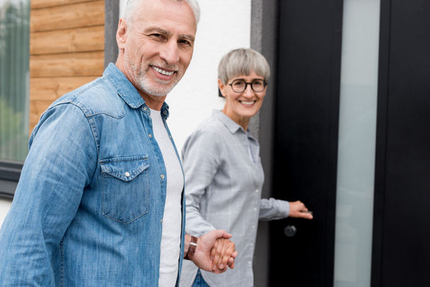 Lächelnde Frau hält Händchen mit Mann und betritt neues Haus  - Foto, Bild