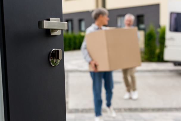 selective focus of door and mature man and woman bringing boxes to new house on background  - Photo, Image