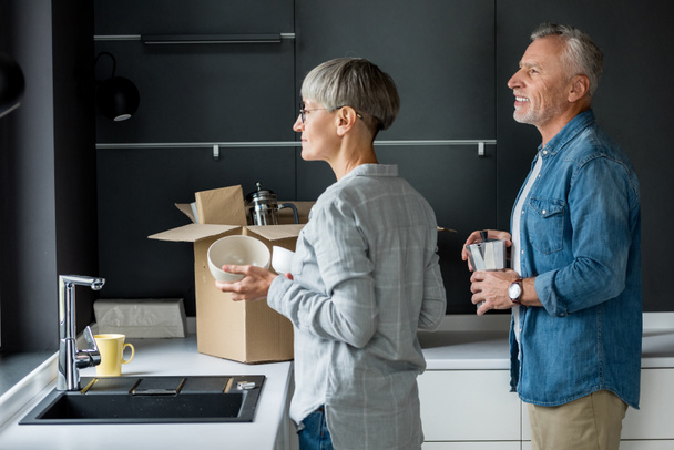 mature man and woman unpacking box in new house  - Fotoğraf, Görsel