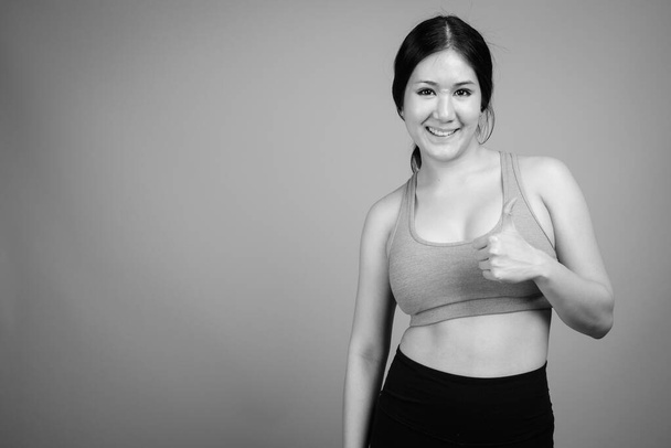 Young beautiful Asian woman ready for gym against gray background - Photo, Image