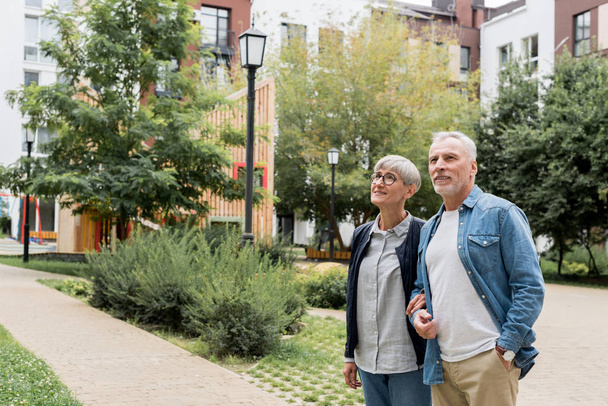 mature man and smiling woman looking away near new buildings  - Photo, Image