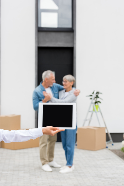 selective focus of broker holding digital tablet and couple standing near new house on background  - Photo, Image